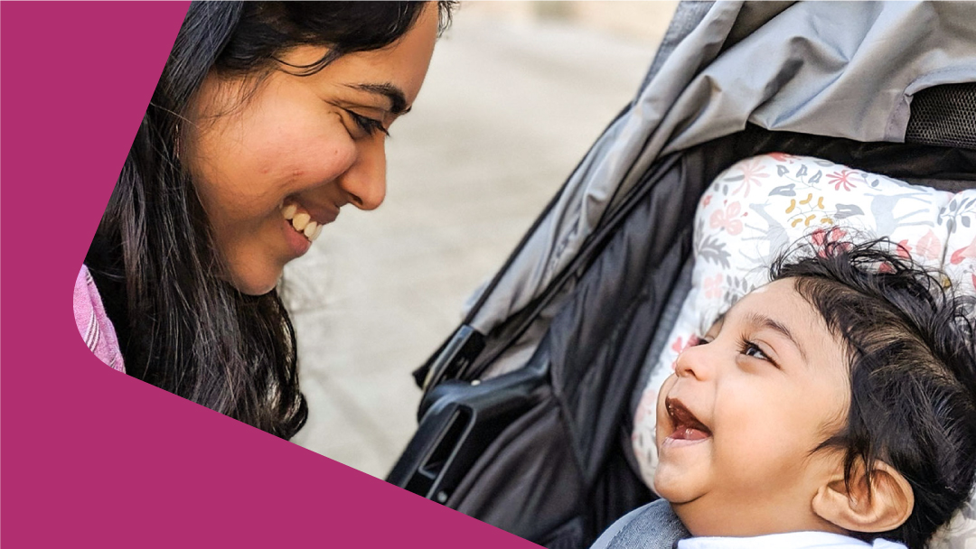 A woman of color smiling at her son in a stroller